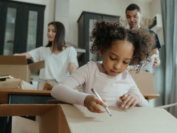 Family unpacking the boxes in their new home, little girl drawing on one of the boxes.