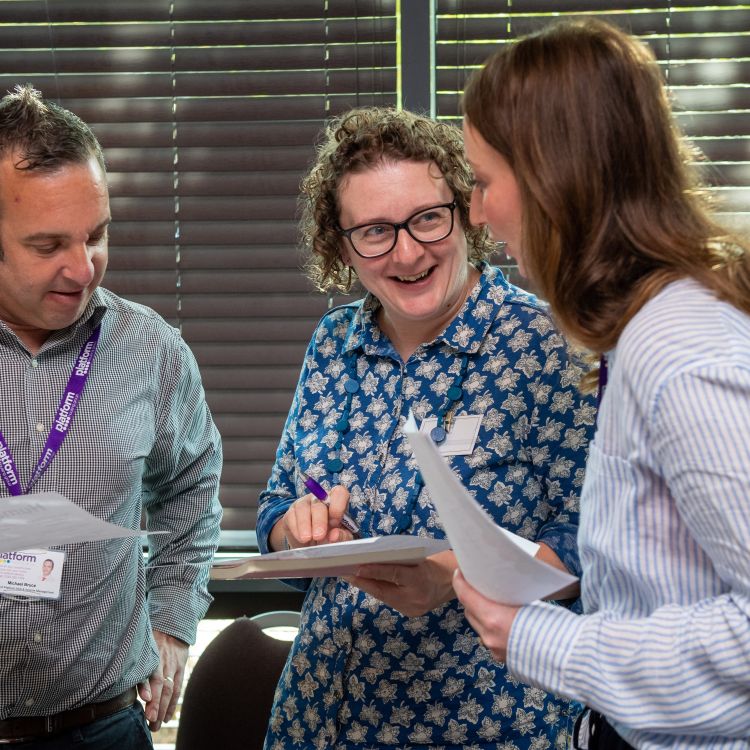 Three colleague stood up talking to each other and smiling